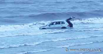 Moment beachgoers watch £35,000 car submerged by sea after getting stuck on the sand