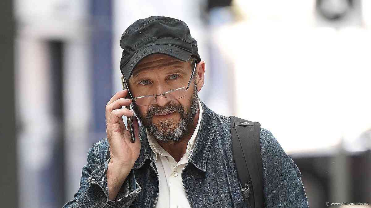 Ralph Fiennes is barely recognisable with a full beard, glasses and a baseball cap as he catches a train at Newcastle Station