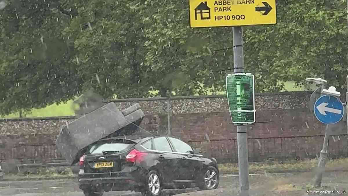 Moment sofa tied to the roof of a car 'with a single piece of string' flies off and hits the road as dopey driver navigates a roundabout