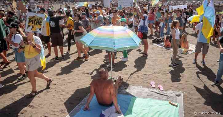 Holidaymakers look on as anti-tourism protesters march across the Canary Islands