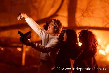 Gleeful young adults grin for selfies while deadly California wildfires roar behind them