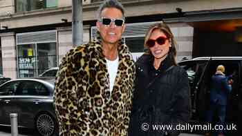 Robbie Williams poses in an eye-catching leopard print coat as he cosies up next to his wife Ayda Field in New York City - days after they were forced to flee LA amid wildfires